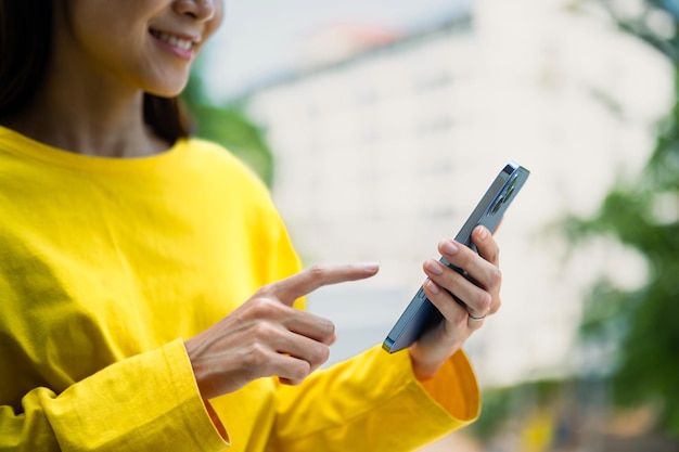 Piacevole giovane donna che invia messaggi di testo in chat sui social sullo smartphone mentre si trova all'aperto