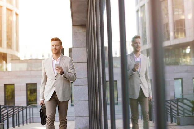 Piacevole uomo alla moda che guarda in lontananza e tiene un telefono cellulare mentre si cammina all'aperto