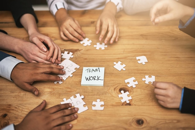 Pianificare tutto pezzo per pezzo Inquadratura dall'alto di un gruppo di colleghi irriconoscibili che costruiscono un puzzle sul tavolo della sala riunioni