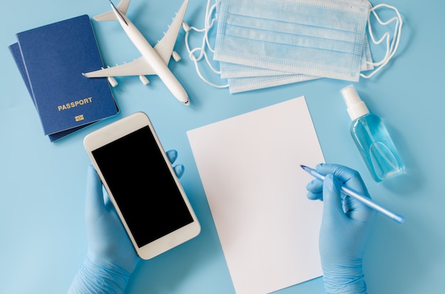 Pianificazione di viaggi e turismo dopo Coronavirus e Quarantena. Le mani in guanti monouso tengono lo smartphone. Manichino con spazio di copia. Modello di aeroplano, passaporti, maschera per il viso e spray disinfettante per le mani.