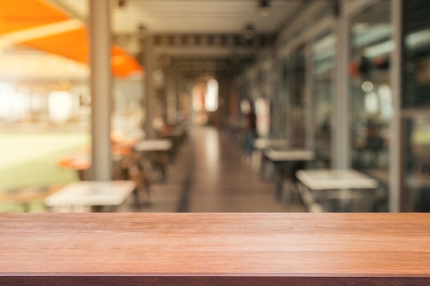 Piano d&#39;appoggio vuoto del bordo di legno sopra di fondo vago. La tavola di legno marrone di prospettiva sopra sfuocatura nel fondo della caffetteria - può essere usata derisione su per i prodotti del montaggio visualizzi o progetti la disposizione visiva chiave.