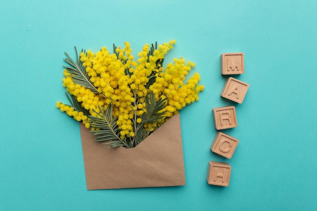 Pianta di mimosa in fiore con fiori gialli in una busta artigianale e iscrizione marzo su cubi di legno su sfondo blu