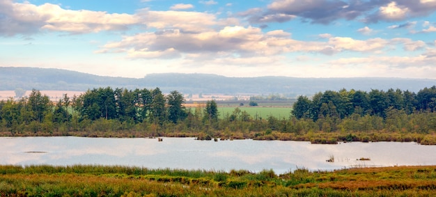 Pianura con fiume e alberi sulla riva del fiume sotto il cielo con pittoresche nuvole in autunno