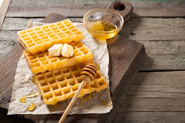 Piastra con deliziosi waffle al miele e una fetta di burro. Su uno sfondo di legno