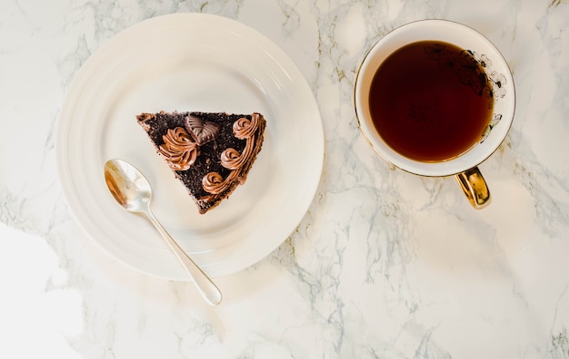 Piastra con fetta di torta al cioccolato fatta in casa e oro giallo tazza di tè su sfondo marmo.spazio copia. Vista dall'alto. Concetto di colazione per le vacanze di Natale Capodanno