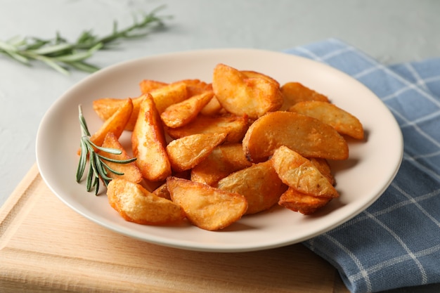 Piastra con fette di spicchi di patate al forno, tovagliolo su grigio. Avvicinamento