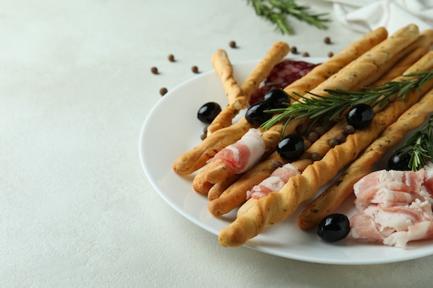 Piastra con grissini e snack su sfondo bianco con texture