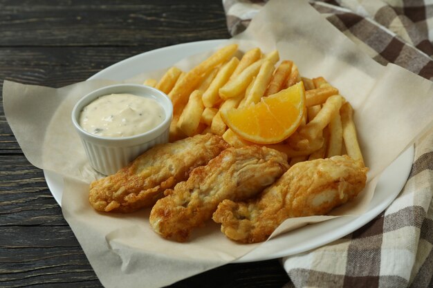 Piastra con pesce fritto e patatine fritte su fondo di legno con carta da cucina