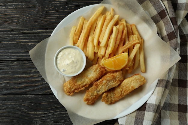 Piastra con pesce fritto e patatine fritte su legno con carta da cucina