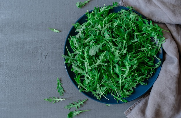 Piastra con rucola fresca verde su sfondo grigio