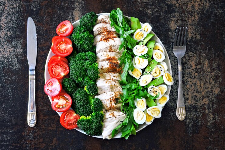Piastra con un alimento dieta cheto. Un insieme di prodotti per la dieta chetogenica su un piatto. Pomodorini, broccoli bolliti, petto di pollo al vapore, insalata con rucola, avocado e uova di quaglia. Pranzo di Keto.