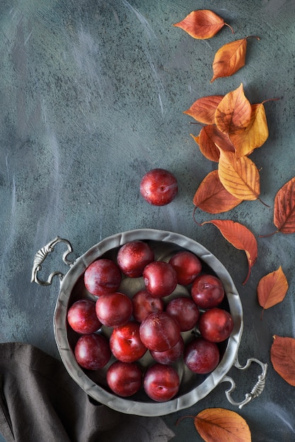 Piastra di metallo vintage con prugne rosse e foglie di autunno sparse rosse e arancioni, piatto giaceva con lo spazio del testo