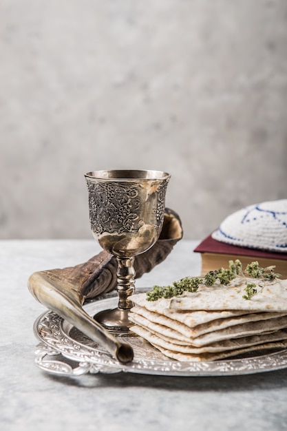 Piastra metallica con matzah o matza, Kiddush Cup, corno Shofar su uno sfondo chiaro presentato come festa seder pasquale o pasto con spazio di copia. Oggetti tradizionali ebraici, yarmulke, Tallit, Libro di preghiere