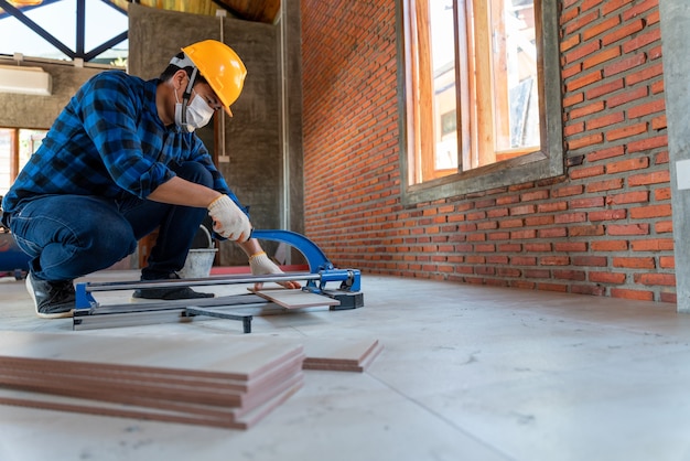 Piastrellista artigiano asiatico in cantiere, lavoratore taglia una grande lastra di piastrelle durante la costruzione di una casa, attrezzatura per il taglio di piastrelle per pavimenti