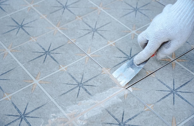 Piastrellista che posa la piastrella di ceramica sul pavimento. Stuccatura di piastrelle ceramiche. Il lavoratore professionista fa renova