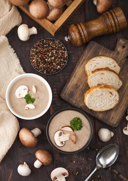 Piatti in ceramica di zuppa di funghi champignon cremosa di castagne con cucchiaio di pepe e panno da cucina su tavola di legno scuro