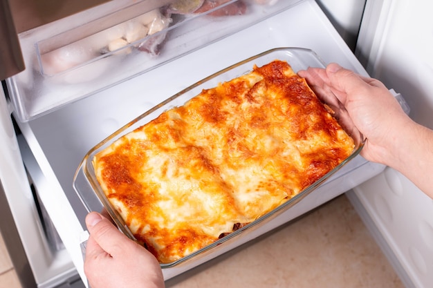 Piatti pronti surgelati. Le mani dell'uomo stanno prendendo le lasagne congelate dal congelatore del frigorifero. Concetto di piatti surgelati pronti e risparmio di tempo sulla cottura degli alimenti.