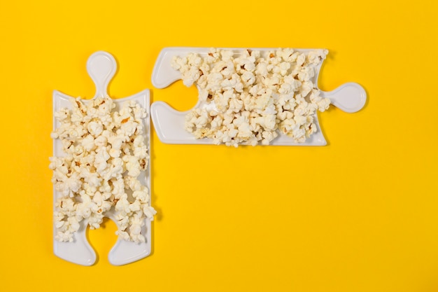 Piatti puzzle con popcorn su sfondo giallo. La migliore compagnia per guardare un film