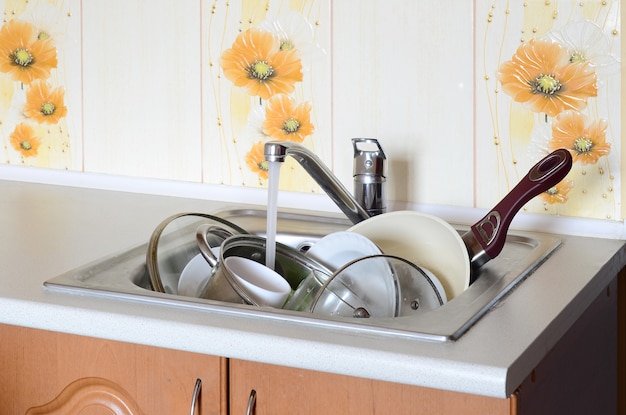 Piatti sporchi e apparecchi da cucina non lavati giacciono nell&#39;acqua schiumosa sotto un rubinetto di un rubinetto della cucina