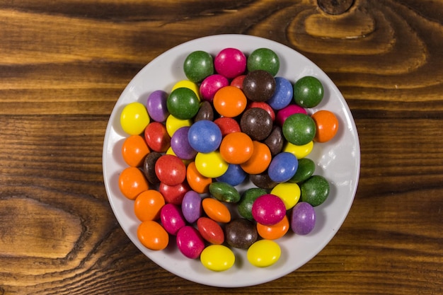 Piattino con caramelle colorate a forma di pulsante ripiene di cioccolato sul tavolo di legno. Vista dall'alto