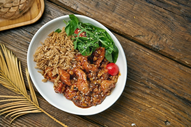 Piatto asiatico - pollo in salsa agrodolce con insalata di rucola e riso in una ciotola su un di legno. cibo di strada