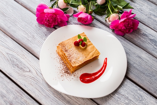 Piatto bianco con dessert. Fiori rosa e bacche rosse. Ricetta francese del dessert estivo. Millefoglie di lamponi con menta.