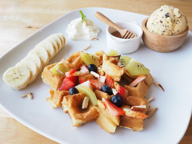 Piatto bianco della cialda con frutta mista e gelato sulla tavola di legno