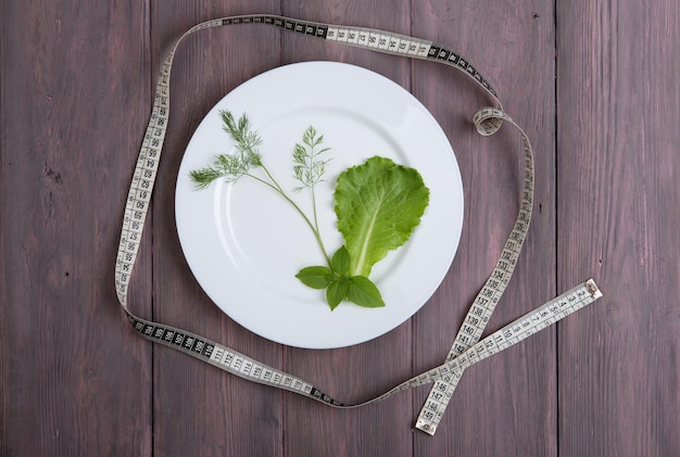 Piatto bianco di concetto di dieta con basilico di lattuga di insalata di aneto e nastro di centimetro