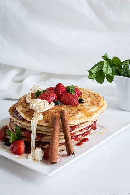 Piatto bianco pieno di pancake con lamponi fragole mirtilli e miele