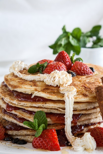 Piatto bianco pieno di pancake con lamponi fragole mirtilli e miele