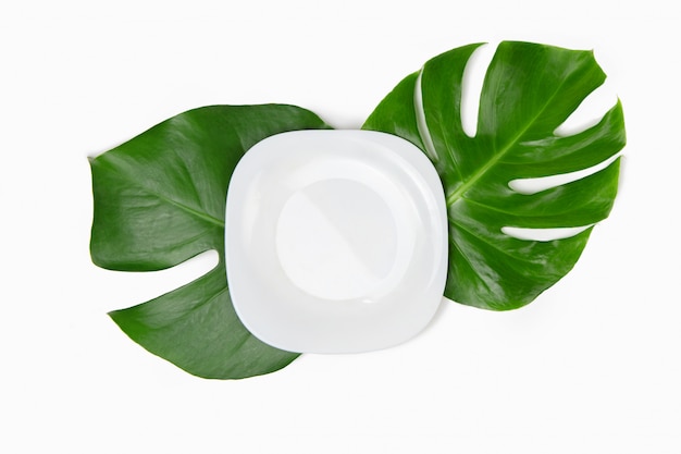 piatto bianco vuoto sopra le foglie di monstera.