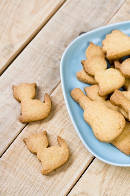 Piatto blu con gustosi biscotti a forma di figurine di gatti e chitarre sul tavolo di legno non verniciato