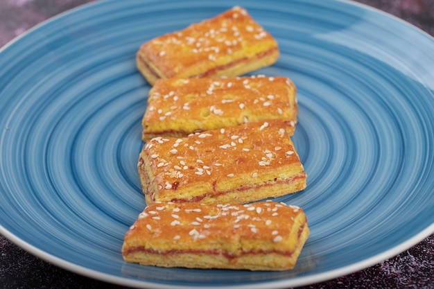 Piatto blu di biscotti con semi di sesamo sul tavolo viola.