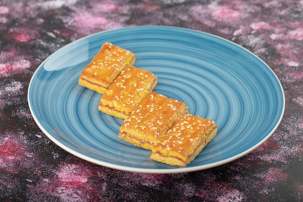 Piatto blu di biscotti con semi di sesamo sul tavolo viola.