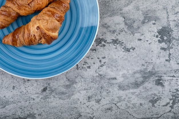 Piatto blu di croissant al cioccolato fresco sulla superficie della pietra.