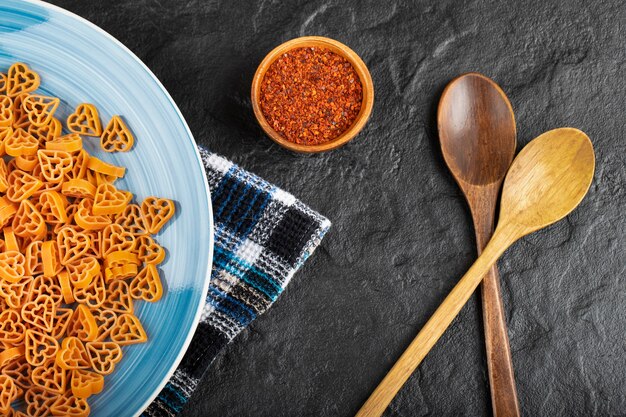 Piatto blu di pasta secca cruda con spezie su sfondo nero.