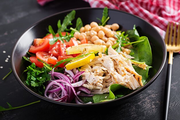 Piatto Buddha bowl con filetto di pollo, ceci, pomodori, cipolla rossa, insalata verde fresca e semi di sesamo. Mangiare sano ed equilibrato.