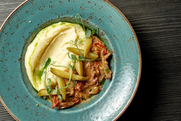 Piatto classico della cucina russa Manzo alla Stroganoff con purè di patate in un piatto blu su fondo di legno