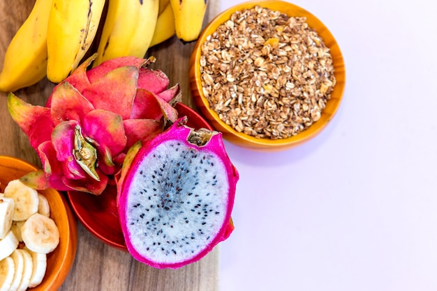 Piatto con banane a fette, muesli e pitaya tagliati a metà. Vista dall'alto.