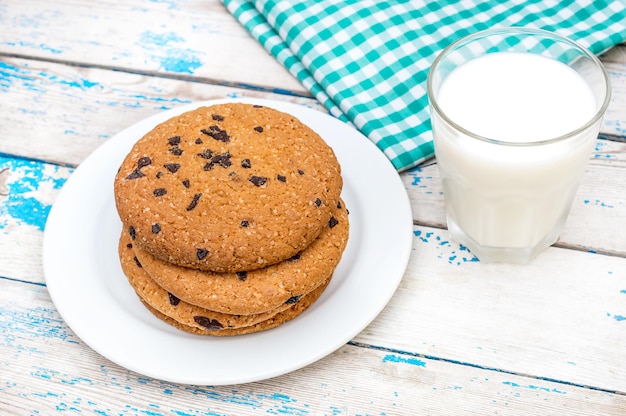 Piatto con biscotti al cioccolato bicchiere di latte e strofinaccio da cucina sul vecchio tavolo di legno blu