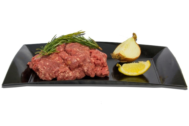 Piatto con carne cruda e decorazioni alimentari intorno su uno sfondo bianco, oggetto isolato