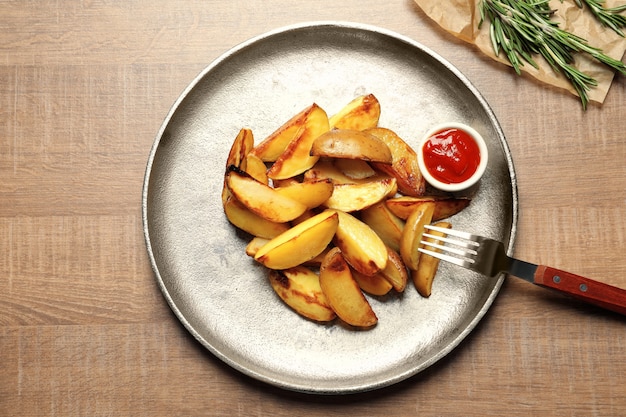 Piatto con deliziosi spicchi di patate al forno e salsa sul tavolo