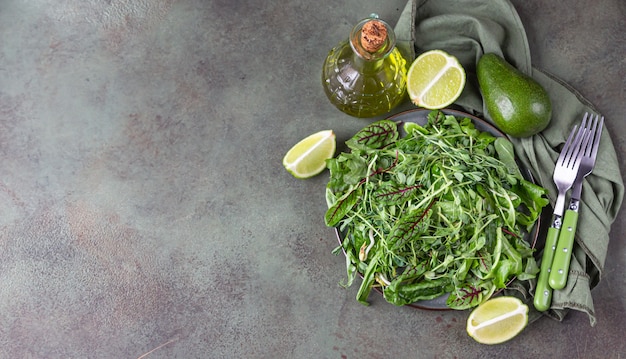 Piatto con foglie di insalata mista e microgreens, lime, avocado e olio d'oliva