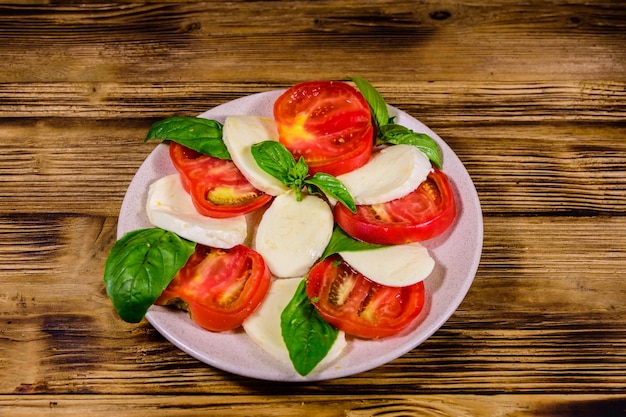 Piatto con insalata caprese insalata italiana con pomodorini mozzarella e foglie di basilico su tavola di legno rustica