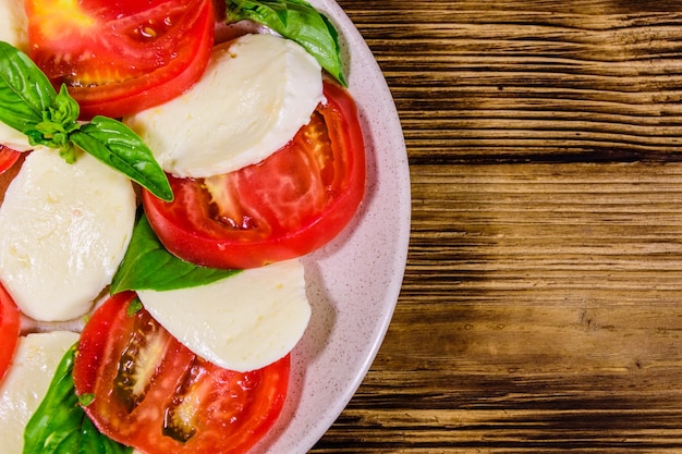 Piatto con insalata caprese Insalata italiana con pomodorini mozzarella e foglie di basilico su tavola di legno rustico Vista dall'alto