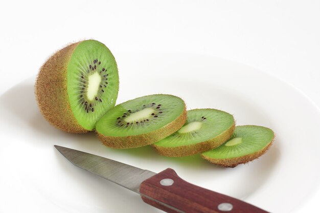 Piatto con kiwi affettato e coltello su sfondo bianco