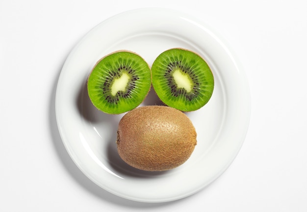 Piatto con kiwi maturi e metà su sfondo bianco, vista dall'alto