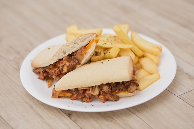 Piatto con panini di carne su pane, con patatine fritte. Sulla tavola di legno.