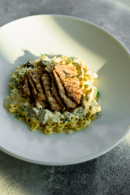 Piatto con pezzi di carne, pasta, verdure, salsa di foie gras e terra verde oliva