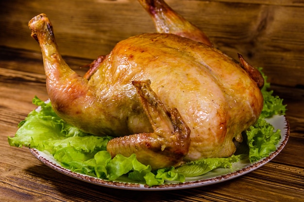 Piatto con pollo intero arrosto e foglie di lattuga su un tavolo di legno